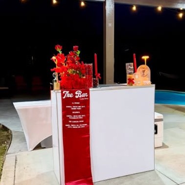 White bar with red roses and a red satin menu runner beside a pool at night