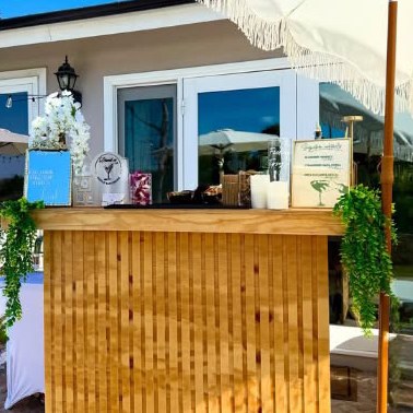 Wooden bar under a fringed umbrella with white orchids and hanging greenery