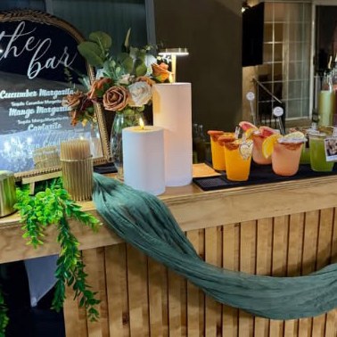 Wooden mobile bar with candles, florals, a draped green runner and a mirrored cocktail menu